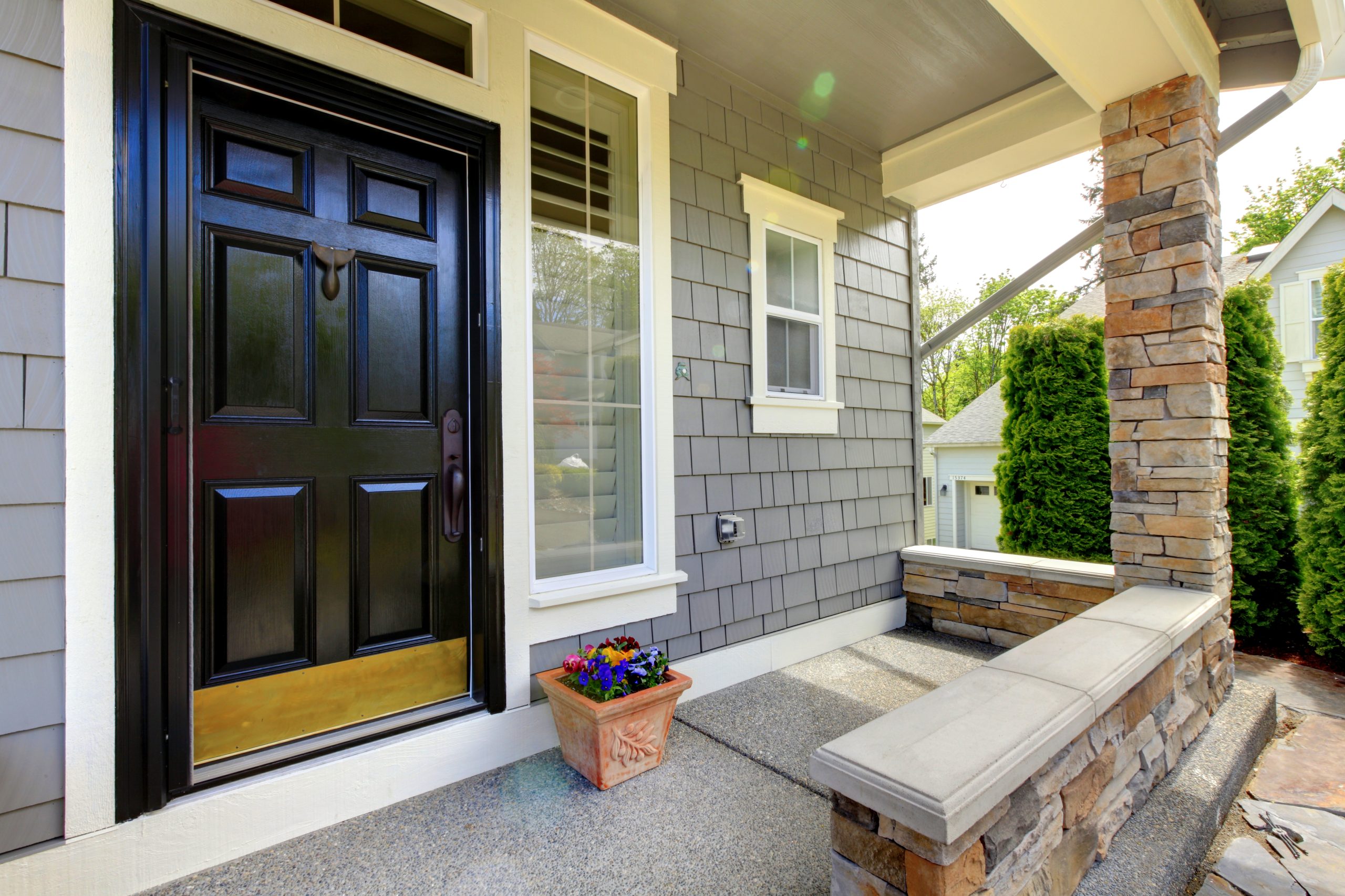 Grey house exterior with black door and stone wall.